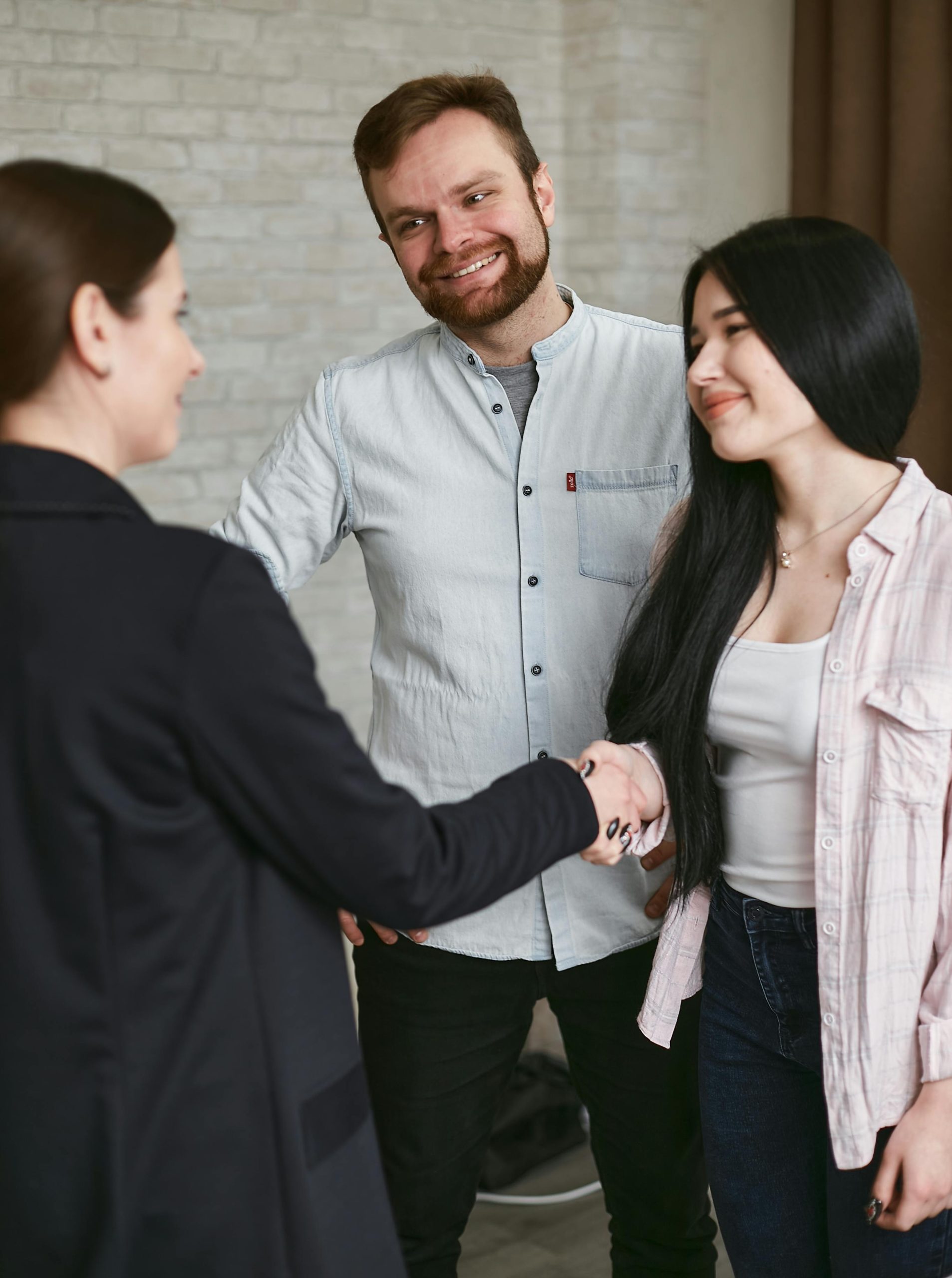 Three adults shaking hands in a professional meeting setting, showing agreement and positive interaction.